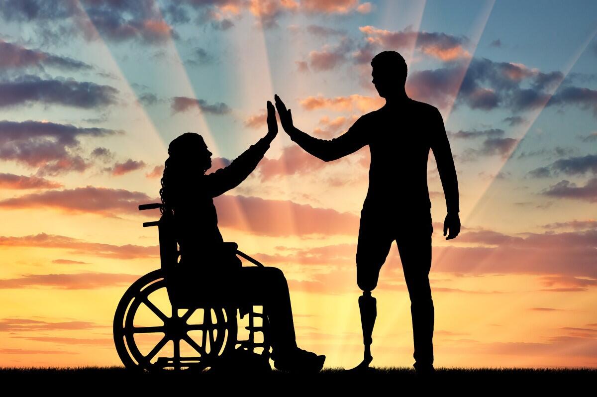 Sunset picture of a woman in a wheelchair high fiving a man with a prosthetic leg